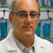 Older man with glasses in a white coat against a lab setting