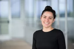 Smiling young woman with hair in bun and black shirt against a blurry office background
