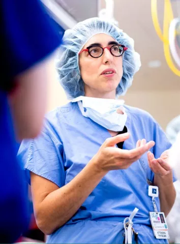 A woman with glasses in scrubs is talking with mask down in lab setting