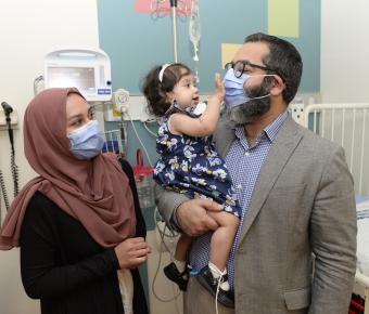 woman and man in mask hold young girl in dress in hospital setting
