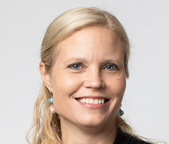 A smiling woman with pulled back medium length blonde hair with black top against a grey background