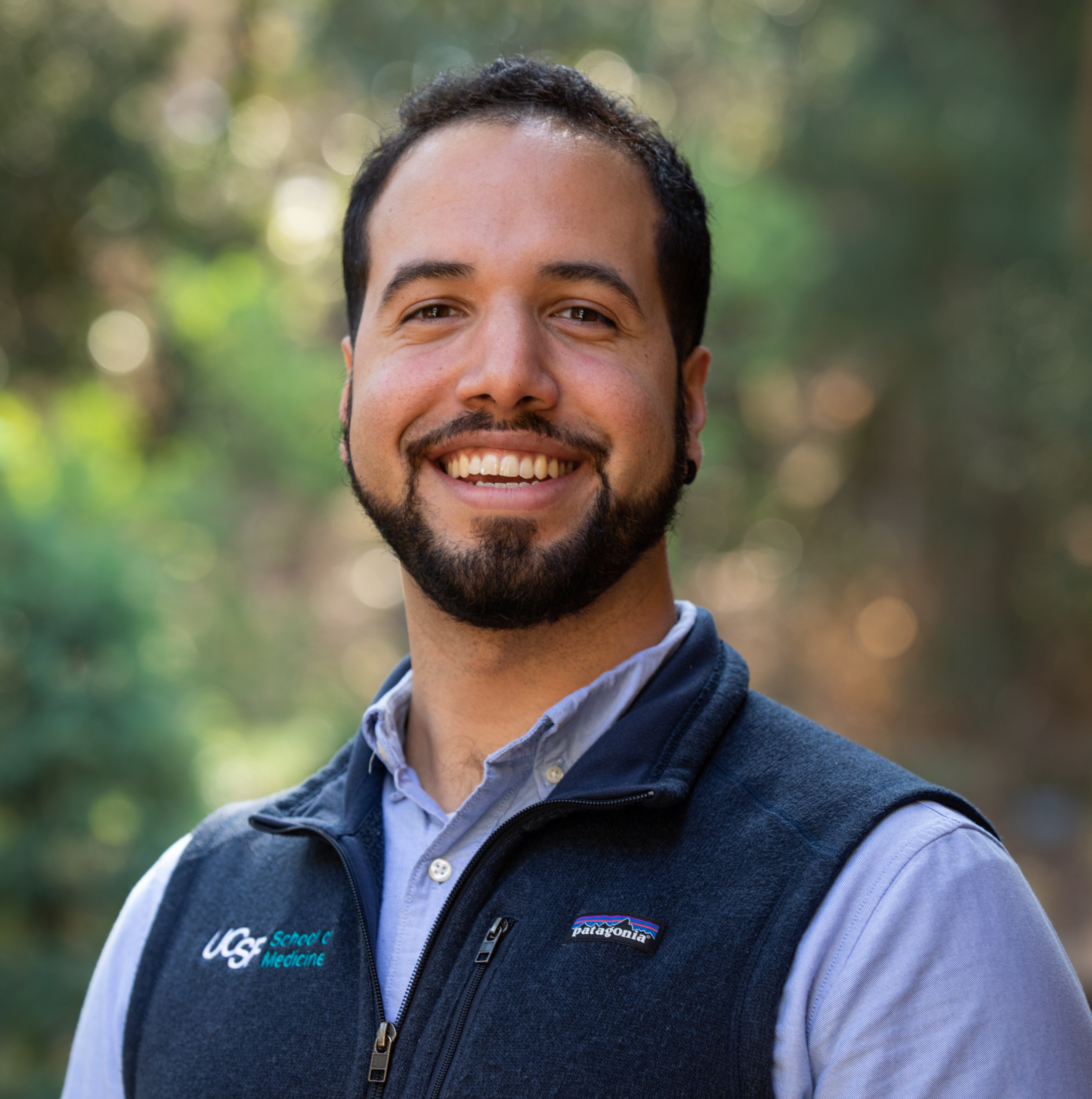 MD-PhD student Ernesto Rojas in outdoor setting dressed in blue vest with blue dress shirt taken by Elisabeth Fall